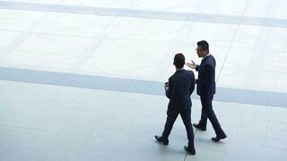 two people in suites walking on a city sidewalk